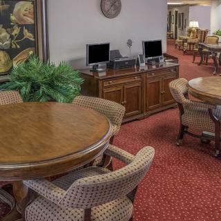 A cozy interior space featuring round wooden tables with chairs, computers on a wooden console, and a red carpet.