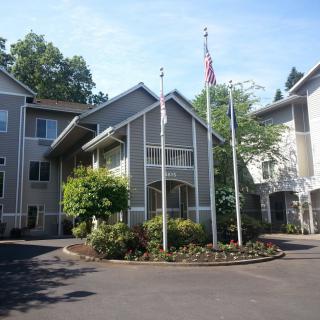 An apartment complex with multiple flags at the entrance surrounded by trees and landscaped gardens.
