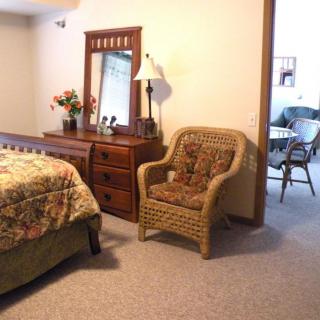 A cozy bedroom featuring a dresser with a mirror, a patterned chair, and a quaint lamp.