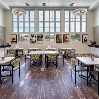 A well-lit dining area with large windows, featuring neatly arranged tables and chairs on a wooden floor.
