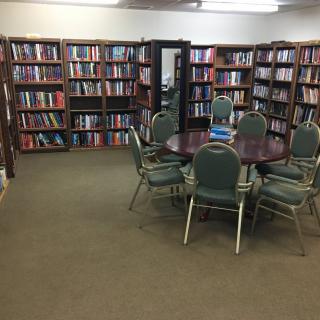 A quiet library space with shelves full of books and a round table surrounded by chairs for studying.