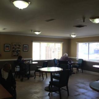 A cozy cafe with several tables and chairs, featuring people seated near large windows.