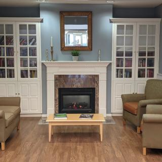 A cozy living room with a central fireplace, flanked by two armchairs and built-in shelves, a small coffee table in front of the fireplace, and a mirror above it.