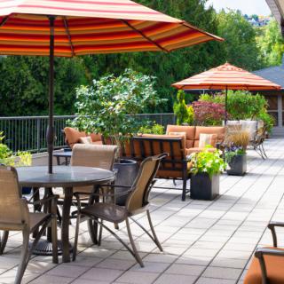 A cozy outdoor patio with tables, chairs, and umbrellas surrounded by lush greenery.