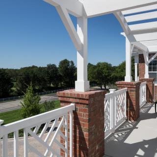 A sunny outdoor balcony with brick columns and white railings overlooking a scenic view.