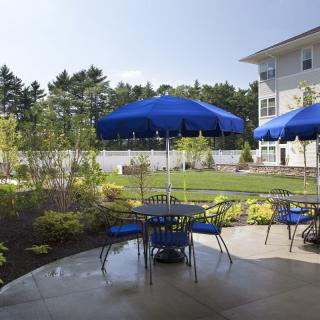 A cozy outdoor patio with blue umbrellas and seating, set in a lush garden on a sunny day.