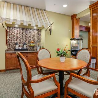 A cozy hotel lobby with a seating area featuring a round table and four chairs, accompanied by a beverage station in the background.