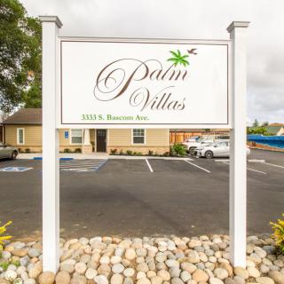 A Palm Villas sign in front of a parking lot and building.