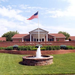 A serene view of a residential home with an American flag and a fountain in the foreground.