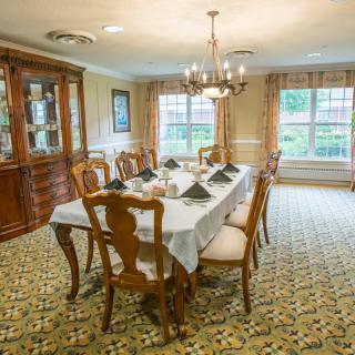 A traditional dining room with a set table, elegant chandelier, and large windows.