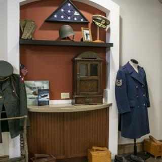 A museum display featuring military uniforms, memorabilia, and an American flag.