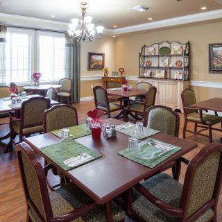 A well-lit dining room with several tables and chairs, decorated with placemats and a chandelier overhead.