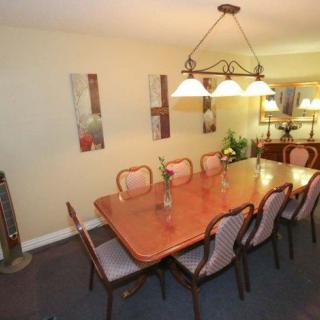 A spacious dining room with a large wooden table and chairs, illuminated by a stylish chandelier.