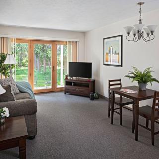 A cozy living room with a seating area, dining table, and large windows overlooking a garden.