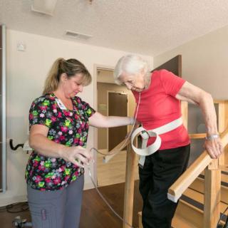 A caregiver assists an elderly woman during a physical therapy session.