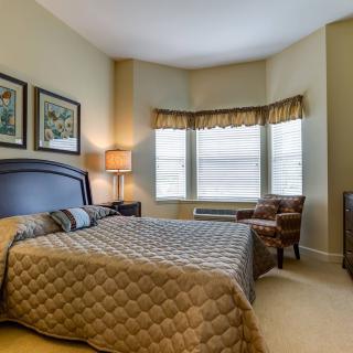 A cozy bedroom with a large bed, two chairs by the window, and warm lighting.