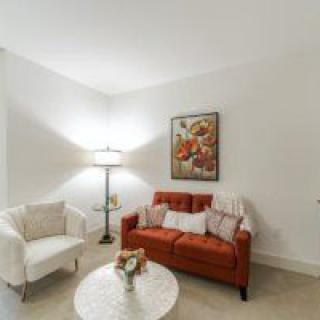 A cozy living room featuring a red sofa, white armchair, floor lamp, coffee table with decor, and wall artwork.