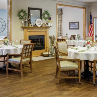 A well-decorated dining area with tables and chairs, featuring a fireplace and an American flag.