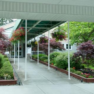 A covered walkway leading to a building, surrounded by lush greenery and vibrant flowers.