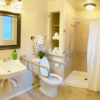 An accessible bathroom featuring a toilet with grab bars, a walk-in shower, sink, and neatly arranged towels.