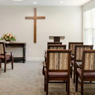 A small chapel with rows of chairs facing a cross on the wall, ready for a religious service.