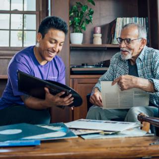 A joyful moment between an elderly man and a young person as they share memories while looking through old documents.
