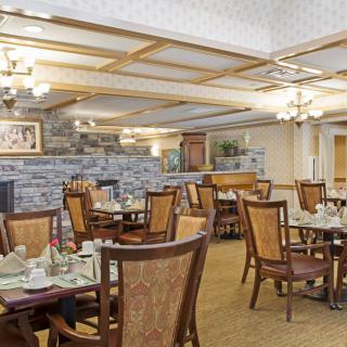 A cozy and elegant dining area with neatly arranged tables and chairs, featuring warm lighting and stone wall accents.