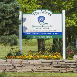 Sign for The Arbors, a memory care facility, with flowers and trees in the background.