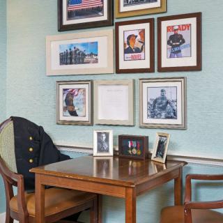 A cozy home office corner with a wooden desk, chairs, and framed pictures on the wall.