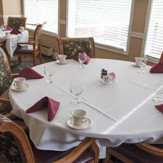 A set dining table with white tablecloth and neatly arranged napkins, cups, and utensils in an elegant restaurant setting.