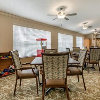 A well-lit dining area featuring multiple tables and chairs, complemented by large windows and ceiling fans.