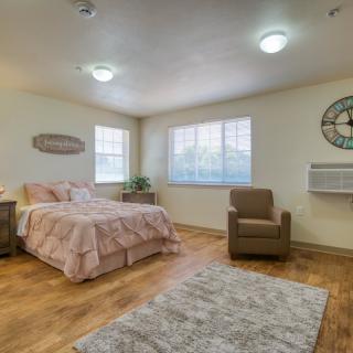 A cozy bedroom featuring a bed, armchair, and large windows.