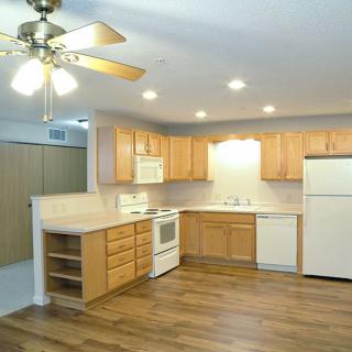 A modern kitchen with wooden cabinets, a ceiling fan, and various appliances including a white refrigerator and stove.