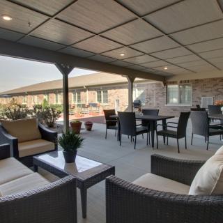 A covered outdoor patio with comfortable seating and a dining area, surrounded by plants.