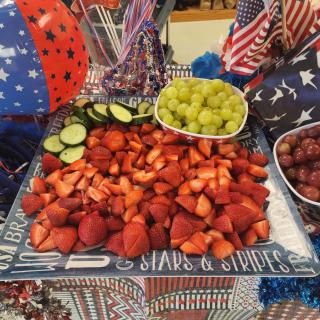 A festive fruit platter with strawberries, grapes, and cucumbers, decorated with American flags for a patriotic celebration.