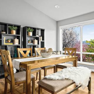 A bright and inviting dining room featuring a wooden table, comfortable seating, and a view of greenery outside.