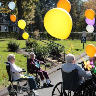 Elderly individuals enjoying a sunny day outdoors, surrounded by colorful balloons.