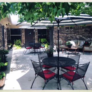 A serene outdoor patio area featuring black iron furniture with red cushions, surrounded by lush greenery.