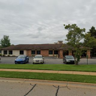 A suburban building with a parking lot and a few parked cars under a cloudy sky.