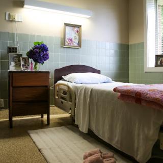 A serene hospital room featuring a neatly made bed, bedside table with flowers, and soft lighting.