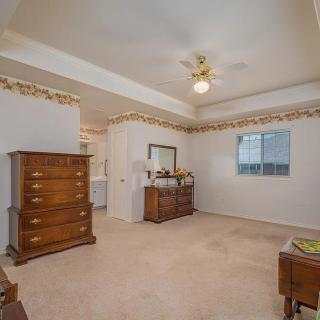 A spacious bedroom with traditional furniture, featuring a dresser and a chest of drawers under a ceiling fan.