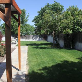 A spacious backyard with a well-maintained lawn and surrounding trees under a clear blue sky.