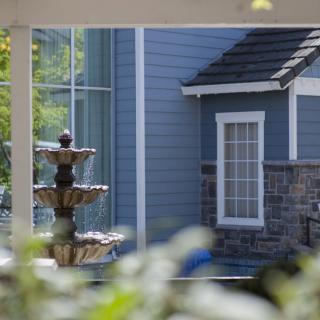 A view of a fountain and the exterior of a blue house with a window, partially obscured by foliage.