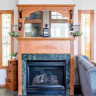 A beautifully designed fireplace with a wooden mantle and green marble base, illuminated by natural light from two windows.