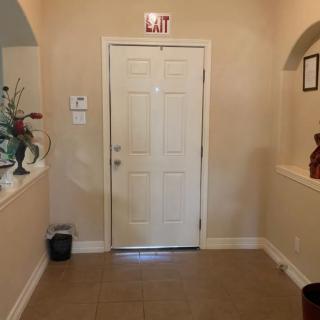 A hallway with a door and an exit sign above, featuring decorative plants on either side.