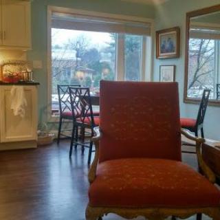 A cozy living room area with a red upholstered chair, large windows, and an adjoining kitchen space.