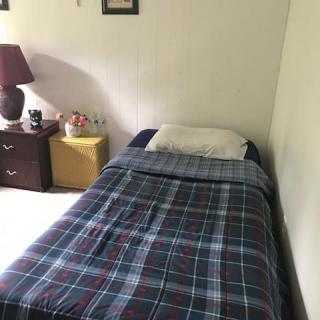A cozy bedroom with a neatly made single bed featuring a plaid blanket, alongside a nightstand with a lamp.
