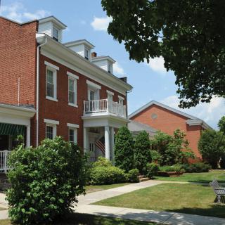 A sunny view of a brick residential building with surrounding trees and a sidewalk.