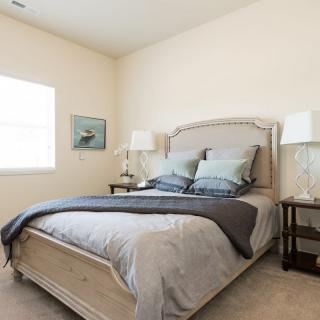 A cozy bedroom featuring a neatly made bed with neutral-colored bedding, flanked by two lamps on side tables.