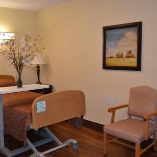 A well-furnished hospital room featuring a medical bed, chair, decorative lamp, and a wall painting.